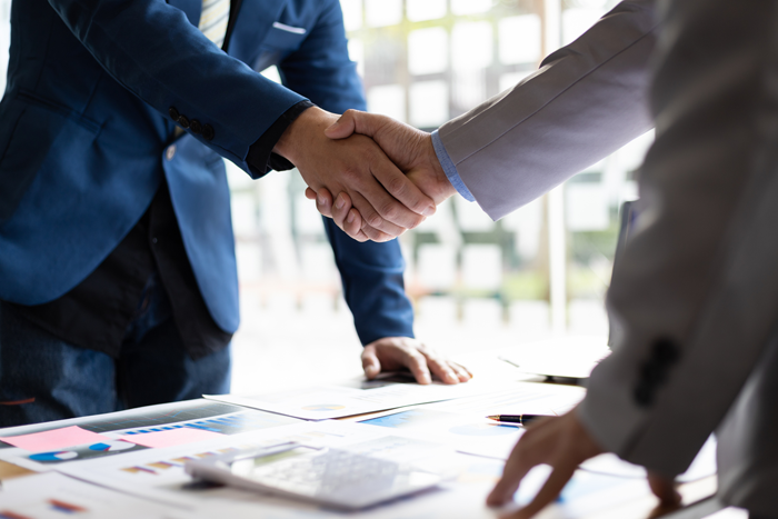 Zwei Geschäftspartner beim Handschlag über einem Tisch mit Vertragsunterlagen – Symbol für Vertrauen und langfristige Zusammenarbeit