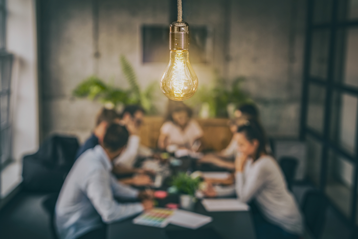Leuchtende Glühbirne als Symbol für Innovation und Ideen, im Hintergrund ein Team bei einer Besprechung